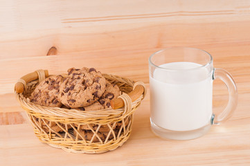 Chocolate cookies in wicker basket and cup of milk on wooden background