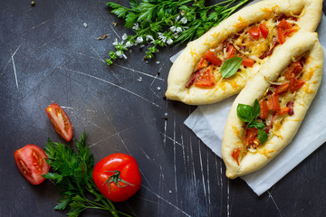 Delicious homemade Greek oval pizza with salami, tomato, onion and cheese on a dark stone background. Copy space.