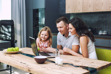 Family mother, father and daughter happy and beautiful with smiles at home together in the kitchen with laptop