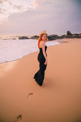 young woman walking along the beach at sunset, rear view
