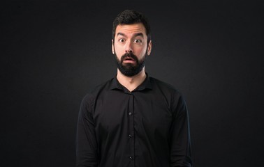 Obraz premium Handsome man with beard making surprise gesture on black background