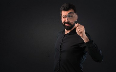 Obraz premium Handsome man with beard with magnifying glass on black background