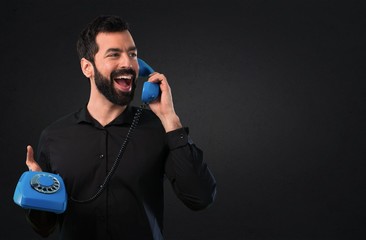 Handsome man with beard talking to vintage phone on black background