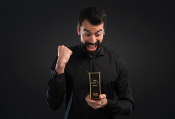 Handsome man with beard with gold ingot on black background