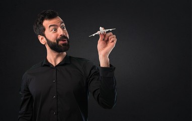 Handsome man with beard holding a toy airplane on black background