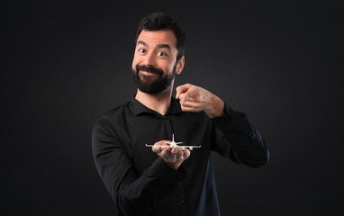 Handsome man with beard holding a toy airplane on black background