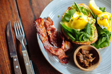 Close up Healthy Breakfast with Wholemeal Bread Toast and Poached Egg with salad, avokado and Beckon on wooden textured table