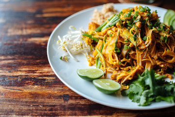 Close up Padthai noodle with smoke tofu and mixed vegetable - wheat germs,lime,cucumber,parsley on wooden textured table.Healthy Vegetarian vegan menu