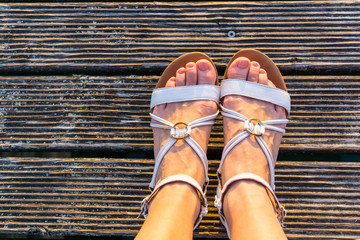 Two beautiful feet of a woman with white sandals in warm sunlight