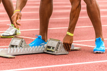 Starting blocks being adjusted by young black male athlete on outdoor track before start of race