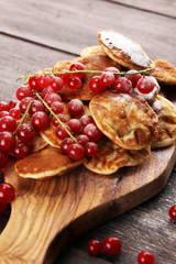 Pancakes or puffertjes with berries and maple syrup on rustic table