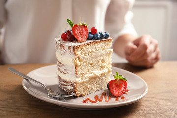 Piece of delicious homemade cake with fresh berries and blurred woman on background