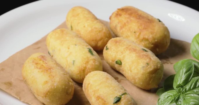 Crocchette di patate infarinate con prezzemolo disposte su un piatto bianco rotante con basilico e formaggio grattugiato. Dieta vegetariana e vegana.