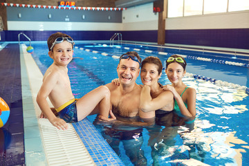 A happy family is smiling in a swimming pool indoors.