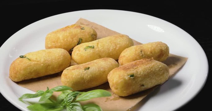 Crocchette di patate infarinate con prezzemolo disposte su un piatto bianco rotante con basilico e formaggio grattugiato. Dieta vegetariana e vegana.