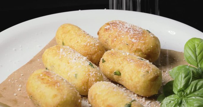 Crocchette di patate infarinate con prezzemolo disposte su un piatto bianco rotante con basilico e formaggio grattugiato. Dieta vegetariana e vegana.