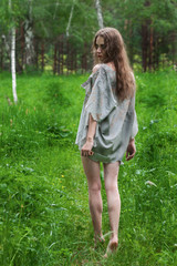 Beautiful young dirty mad and manic looking girl wearing torn clothes and smeared with mud and dried blood is walking with a knife in her hand in the forest