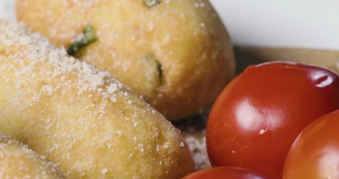 Crocchette di patate infarinate con prezzemolo disposte su un piatto bianco rotante con basilico e formaggio grattugiato. Dieta vegetariana e vegana. Vista macro.