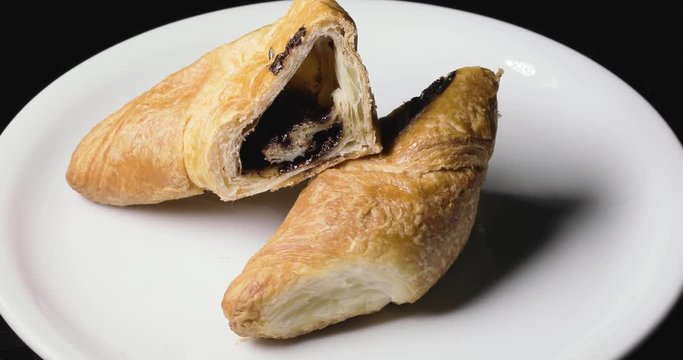 Cornetto caldo al cioccolato per la prima colazione su un piatto bianco rotante. Vista macro.
