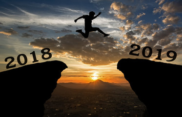 A young man jump between 2018 and 2019 years over the sun and through on the gap of hill  silhouette evening colorful sky. happy new year 2019.