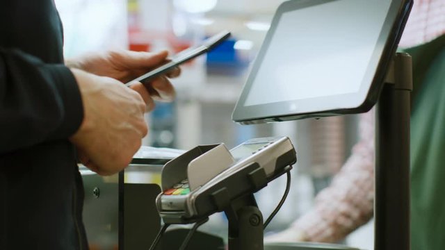 In the Supermarket Close-up Footage of the Man Paying with Smartphone at the Checkout Counter. Using Modern and Convenient Wireless NFC Paying System in Big Mall.