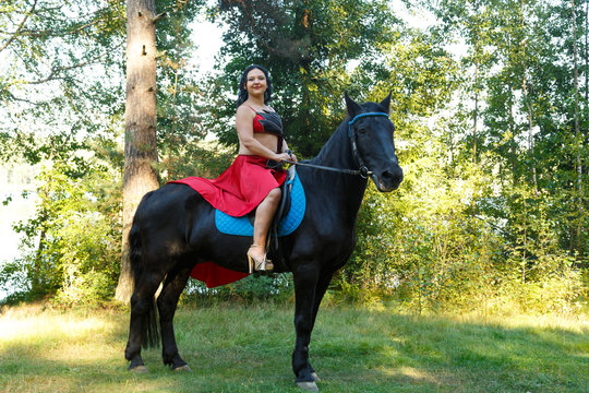 Eastern beauty in a red suit in a saddle on a horse in the forest.