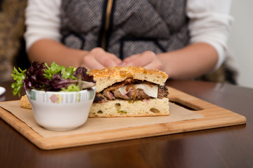 A steak sandwich on focaccia bread with a side salad.