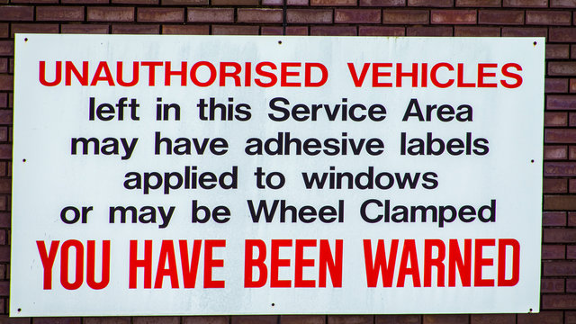 Vehicle wheel clamping warning sign attached to a brick wall.