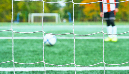 Young blurred soccer player taking a penalty kick against goal net.