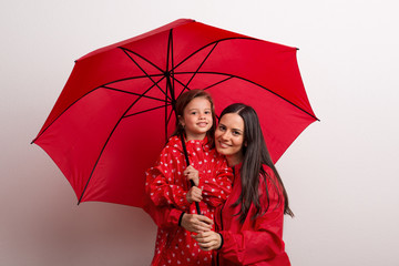 A small girl with her mother under an umbrella on a white background.
