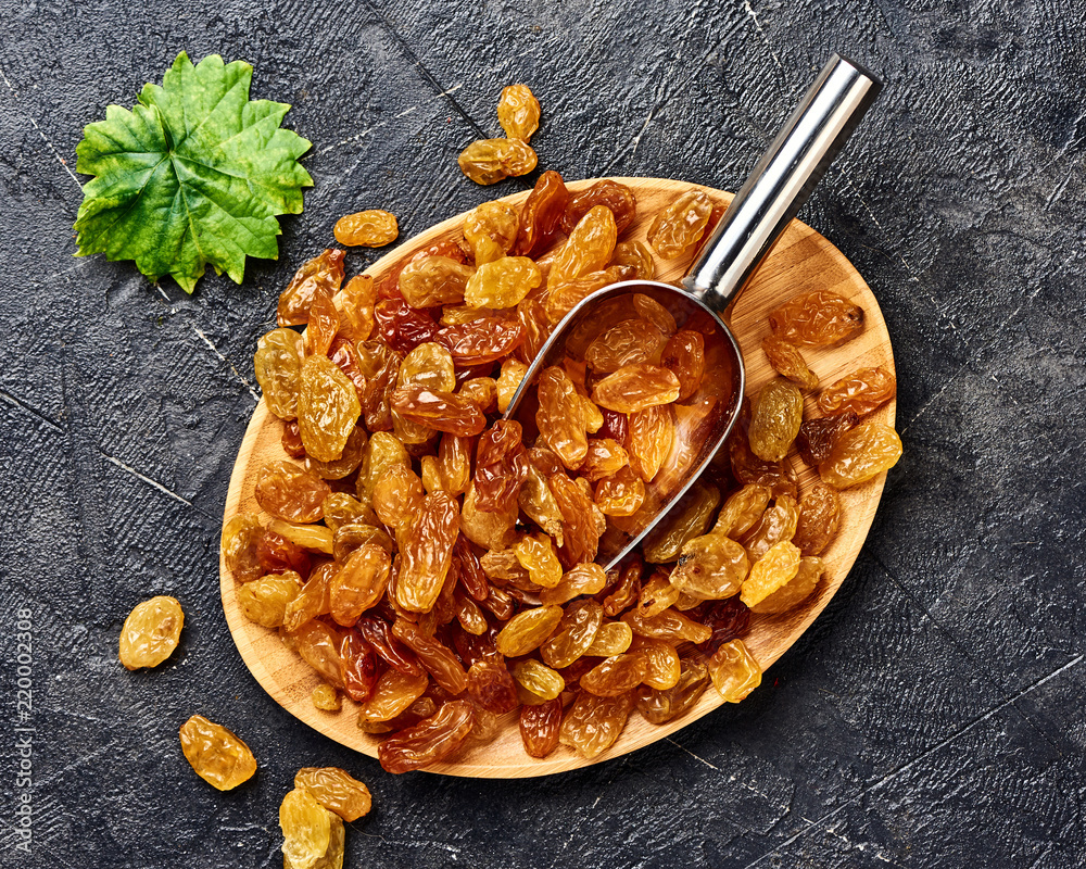 Wall mural Yellow raisins on black concrete background with scoop. Top view of dried grapes.