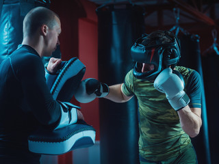 Two Man Fighters training together with punching pads at gym. Guy in protective doing kickboxing workout with her coach.