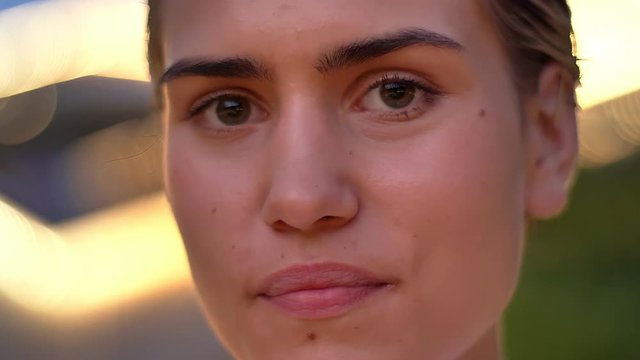 Face of young modern woman is watching at camera in evening, blurred lights on background