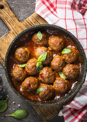 Meatballs in tomato sauce in a frying pan on dark stone table. 