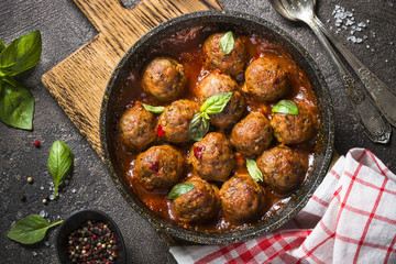 Meatballs in tomato sauce in a frying pan on dark stone table. 