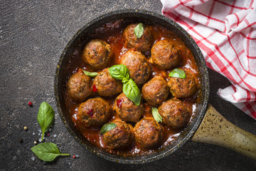 Meatballs in tomato sauce in a frying pan on dark stone table. 