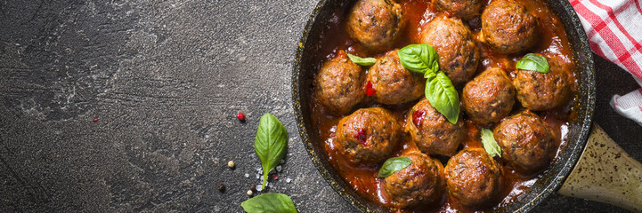 Meatballs in tomato sauce in a frying pan on dark stone table. 
