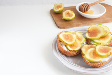 Fresh green figs Wooden cutboard Porcelain plate Wholegrain bread Honey Goat cheese Healthy eating concept Canapes Sandwiches Appetizer Copy space White background