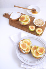 Fresh green figs Wooden cutboard Porcelain plate Wholegrain bread Honey Goat cheese Pine nuts Healthy eating concept Canapes Sandwiches Appetizer Copy space White background Top view