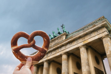 The girl is holding a delicious traditional German pretzel in the hand against the backdrop of the Brandenburg Gate in Berlin, Germany. © franz12