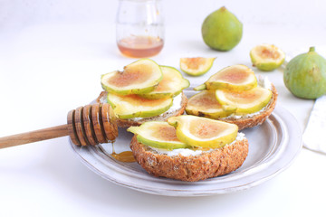 Fresh green figs Porcelain plate Wholegrain bread Honey Goat cheese Healthy eating concept Canapes Sandwiches Appetizer Copy space White background
