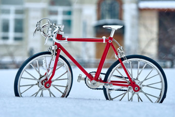 Fototapeta na wymiar A toy model of a red bicycle made of metal, executed with good accuracy, is in winter in snowdrifts and cold weather on a city street