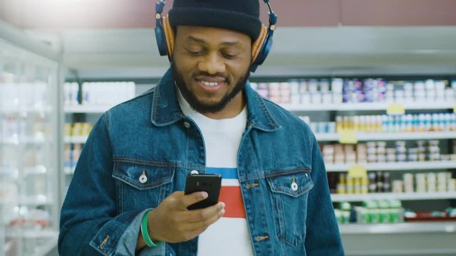 Portrait Shot of the Stylish African American Man Using Smartphone, Listening to a Headphones and Walking Through Supermarket.