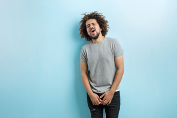 A curly-headed handsome man wearing a gray T-shirt is standing and laughing with his eyes closed...