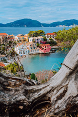 Fototapeta na wymiar Assos village in Kefalonia, Greece. Calm blue bay water and colored traditional houses. Old snag in the front