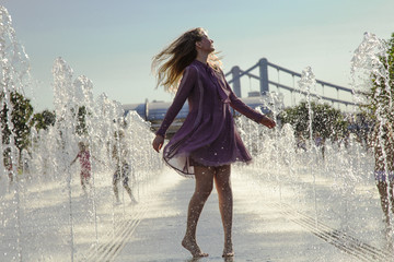the girl in a pink dress dances among the fountains at hot summer day in a city