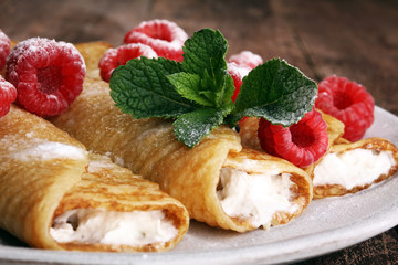 Homemade crepes served with fresh raspberrries and powdered sugar on rustic wooden table
