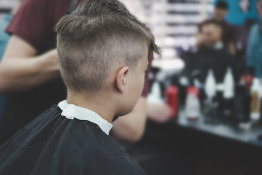 Boy get his hair cutted and groomed in barber shop, rear view retro color