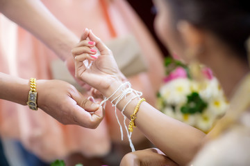 The bride's hand is tied with thread from the older culture in Thai wedding ceremony. bind holy thread with hand in thai rite.