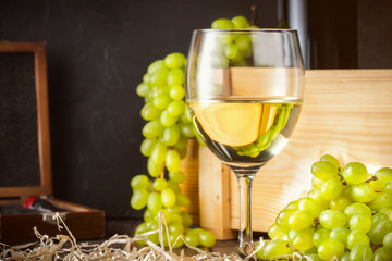 White wineglass and white yellow green bunches of berry grapes with bottle of wine corkscrew for cork on table in winery Concept food agriculture harvesting winemaking autumn summer. - 220014512